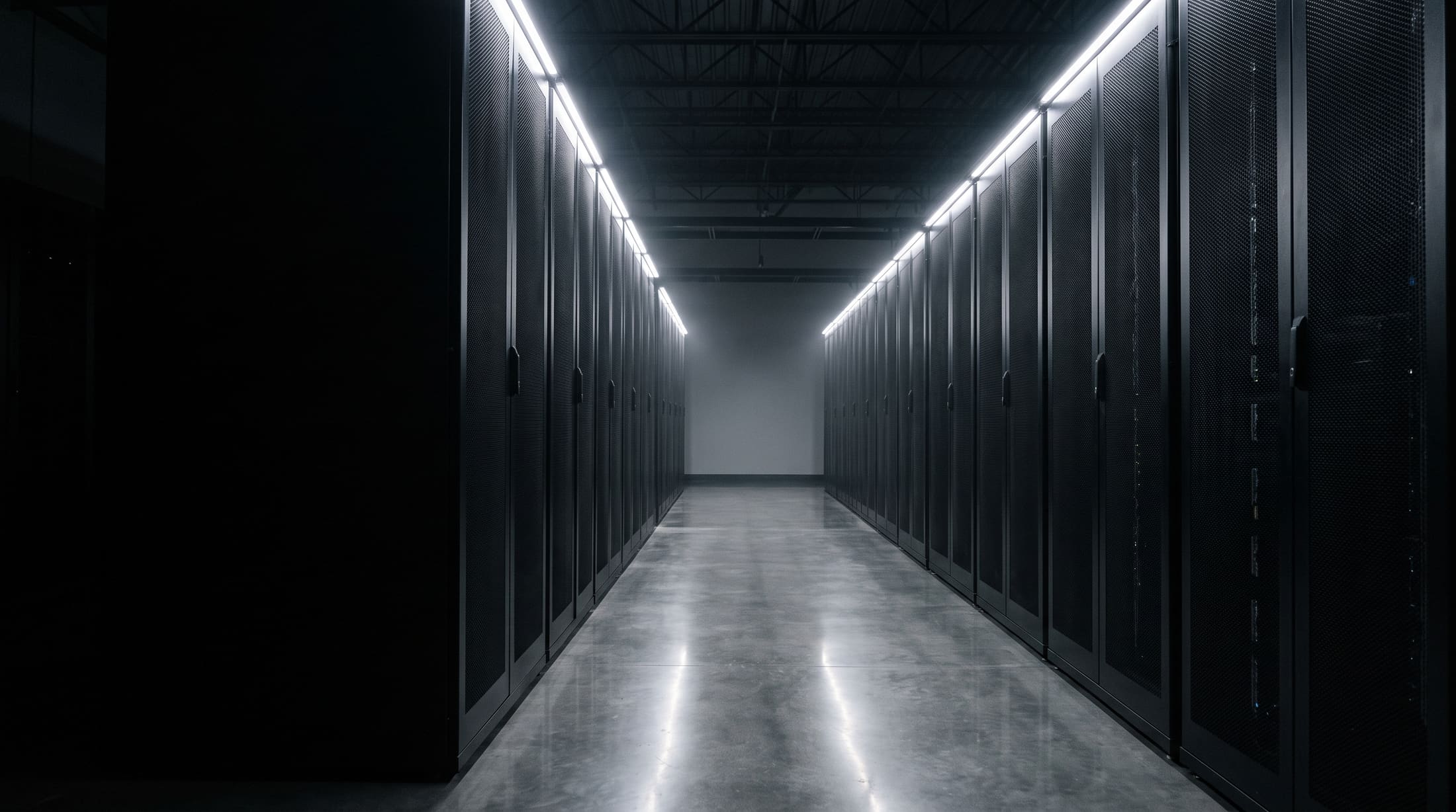 A data centre aisle at night, two rows of server cabinets receding into the dark